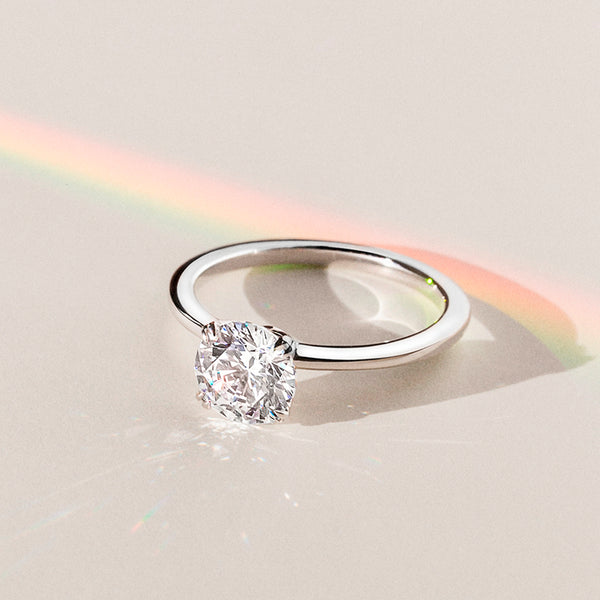 Elodie Whisper enchants with its delicate silhouette and double claw prongs that gently embrace a brilliant round diamond, floating effortlessly atop a slender white gold band.